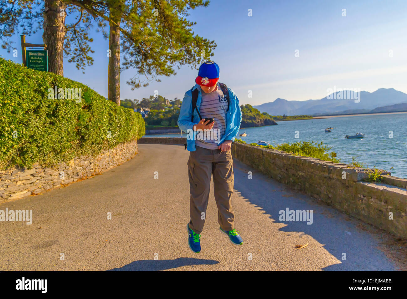 Teenager 'levitating' while checking his mobile phone with the Snowdonia Mountain Range in the background. Stock Photo