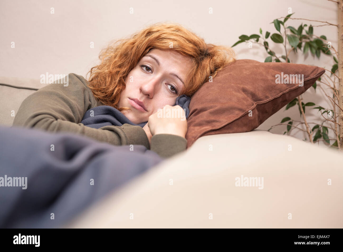 Sad lonely redhead woman resting on the sofa at home. Stock Photo