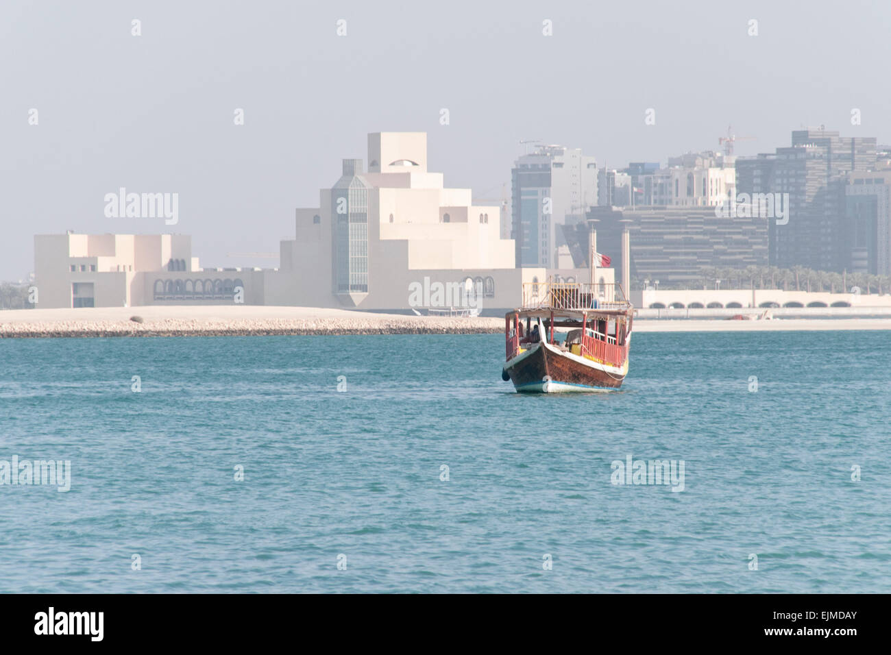 A dhow boat cruises on the Arabian Gulf with the Museum of Islamic art in the background. Doha, Qatar. Stock Photo