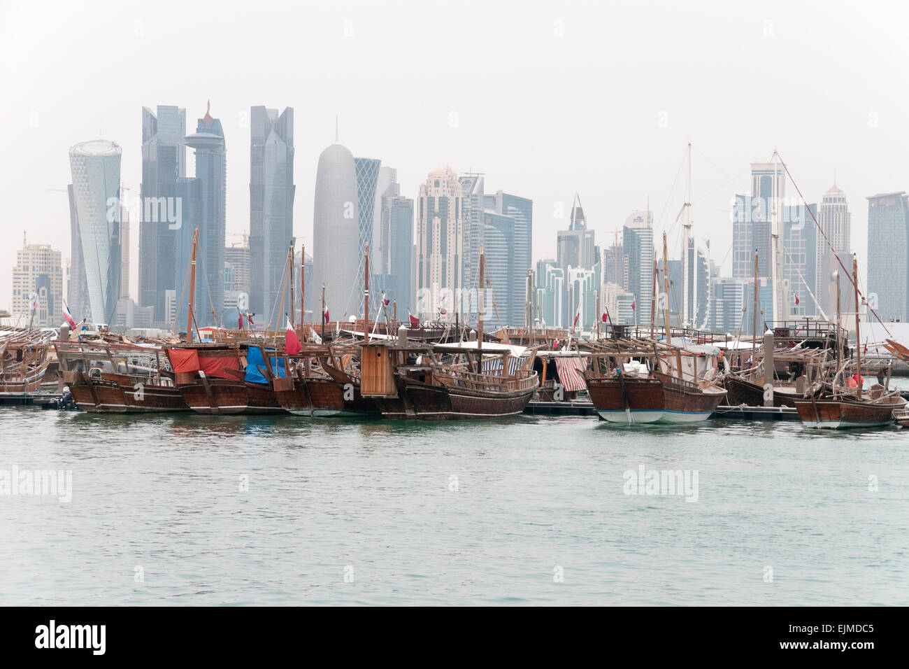 A fleet of dhow boat docked in a port, with the skyline of Doha, Qatar, in the background. Stock Photo