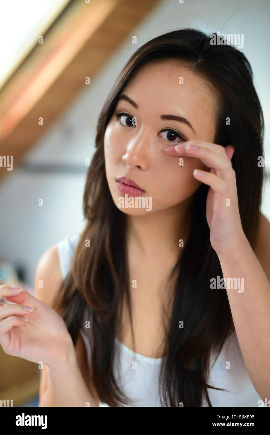 A young slim attractive ethnic chinese asian woman girl wearing white underwear  applying makeup to her face in a bathroom at home UK Stock Photo - Alamy