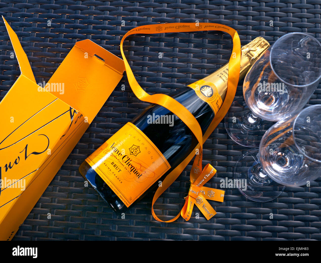 Bottle of Veuve Clicquot luxury Champagne presentation box and glasses on sunny outdoor alfresco wicker table surface Stock Photo