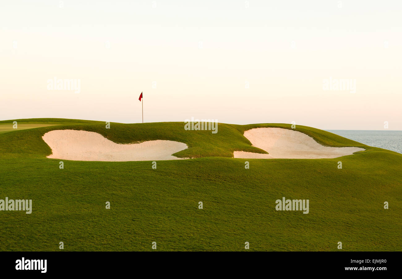 Red flag of golf hole above sand trap or bunker on beautiful ocean ...
