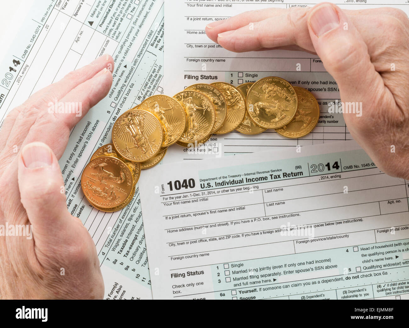 Caucasian hand protecting wealth in solid gold eagle coins on USA tax form 1040 for year 2014 illustrating keeping assets away f Stock Photo
