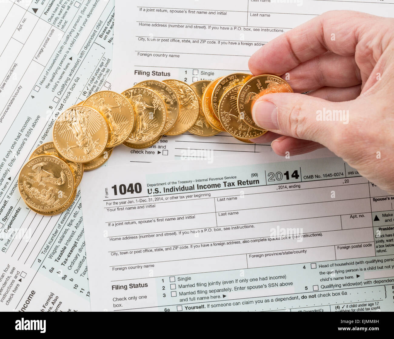 Caucasian hand counting solid gold eagle coins on USA tax form 1040 for year 2014 illustrating payment of taxes to the IRS Stock Photo