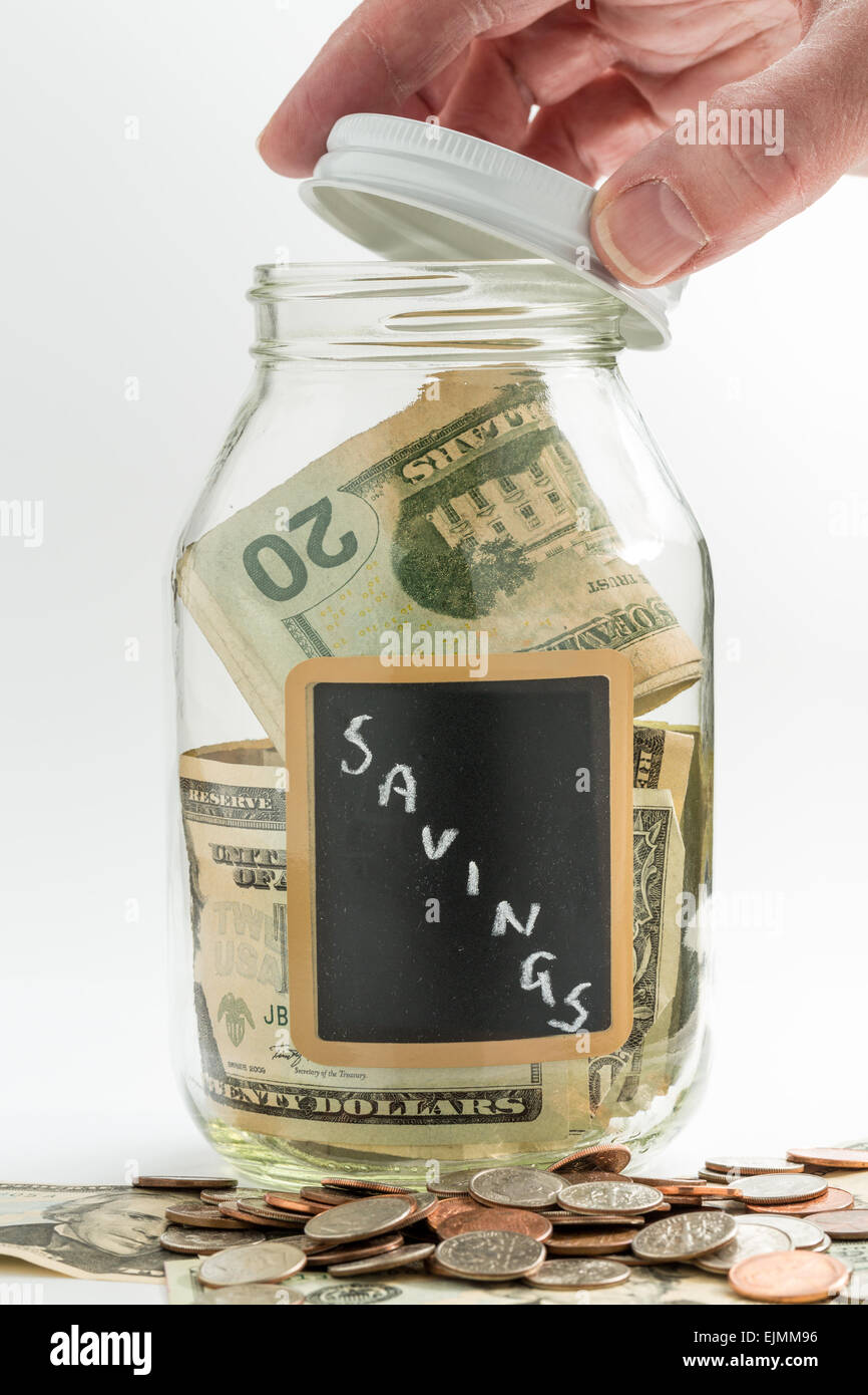 Hand opening lid of glass jar on white background with black chalk label and used for savings US dollar bills Stock Photo