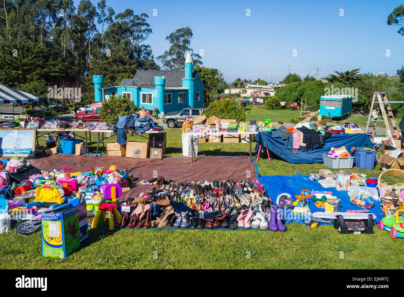 A yard sale in the front lawn of an unusual house shaped like a small castle and painted a turquoise color. Stock Photo