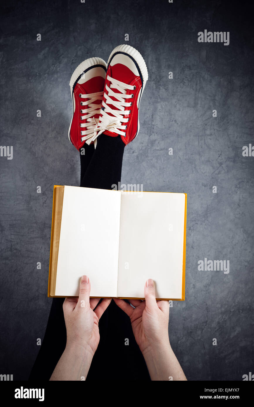 Young Woman Reading Pulp Fiction Book with Her Feet Raised in The Air, Blank Pages as Copy Space. Stock Photo