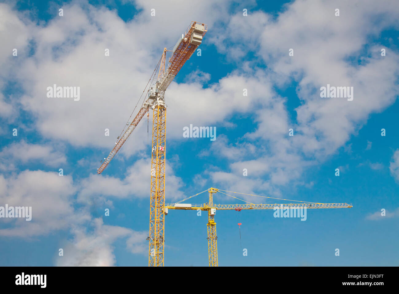 Two yellow construction cranes against beautiful blue sky with clouds Stock Photo