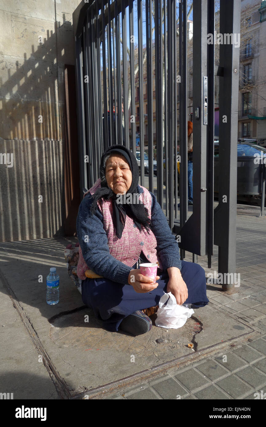 Old woman sitting on ground, begging outside La Boqueria market on Las Ramblas in Barcelona, Catalonia, Spain Stock Photo