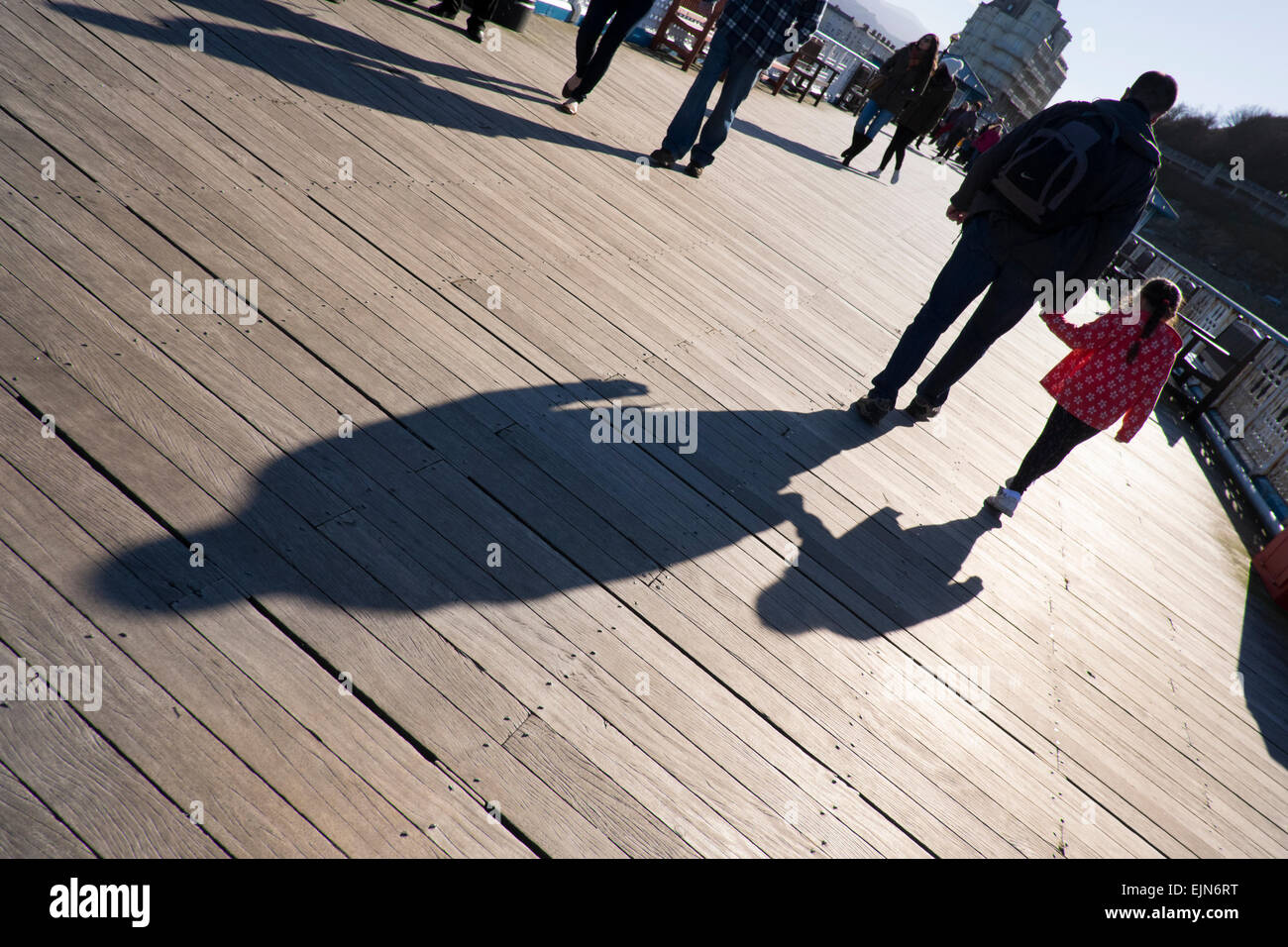 A man and young girl cast shadows as they walk on Llandudno pier, Conwy, Wales, UK Stock Photo