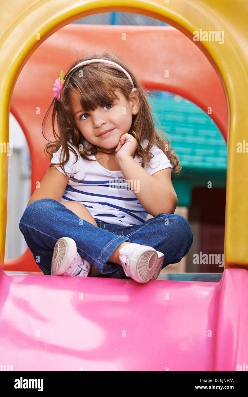 Girl sitting in tailor seat on a slide in a playground Stock Photo