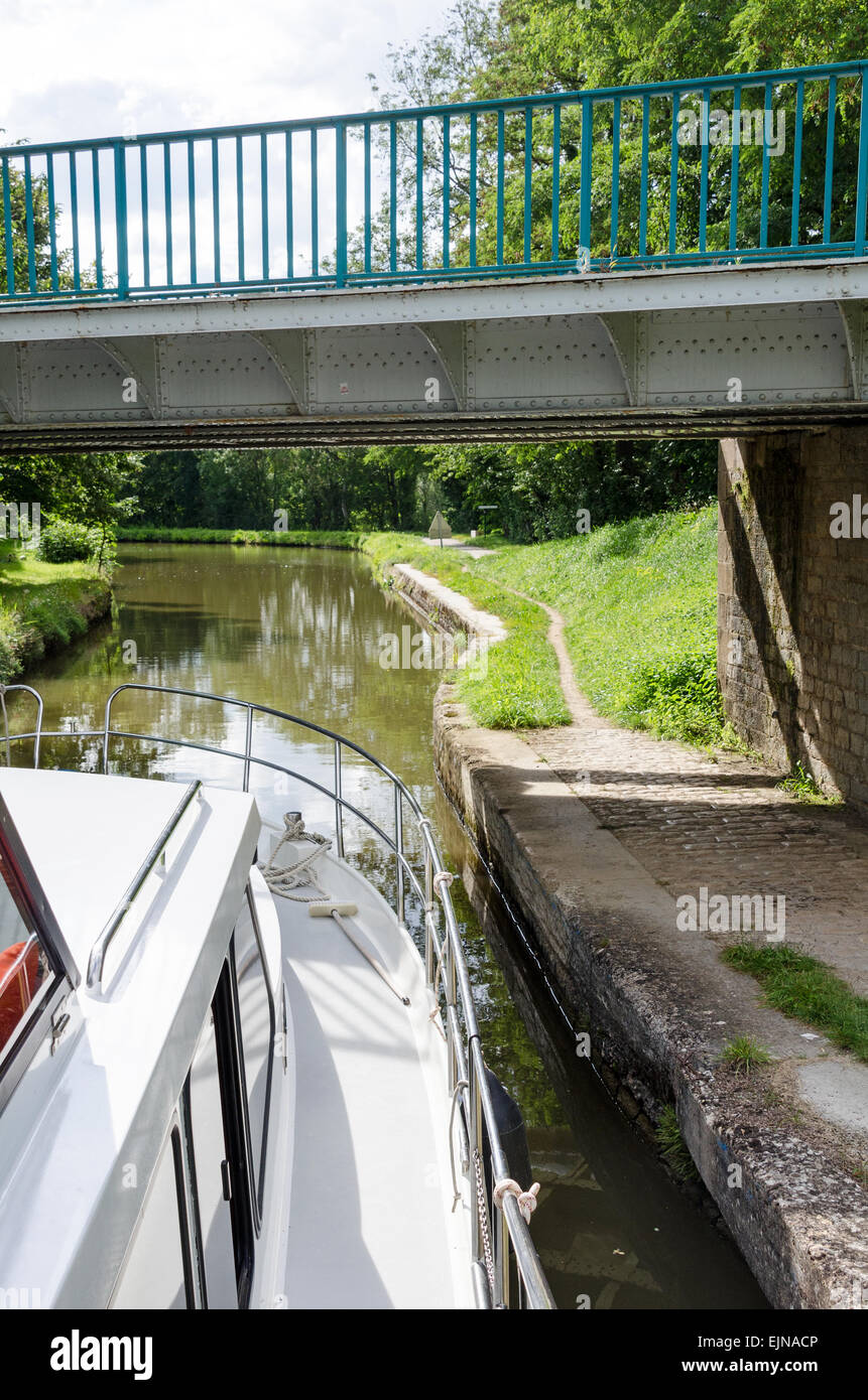 A boat cruises under a low bridge on the historic Canal du Centre near Remigny, Burgundy, France. Stock Photo