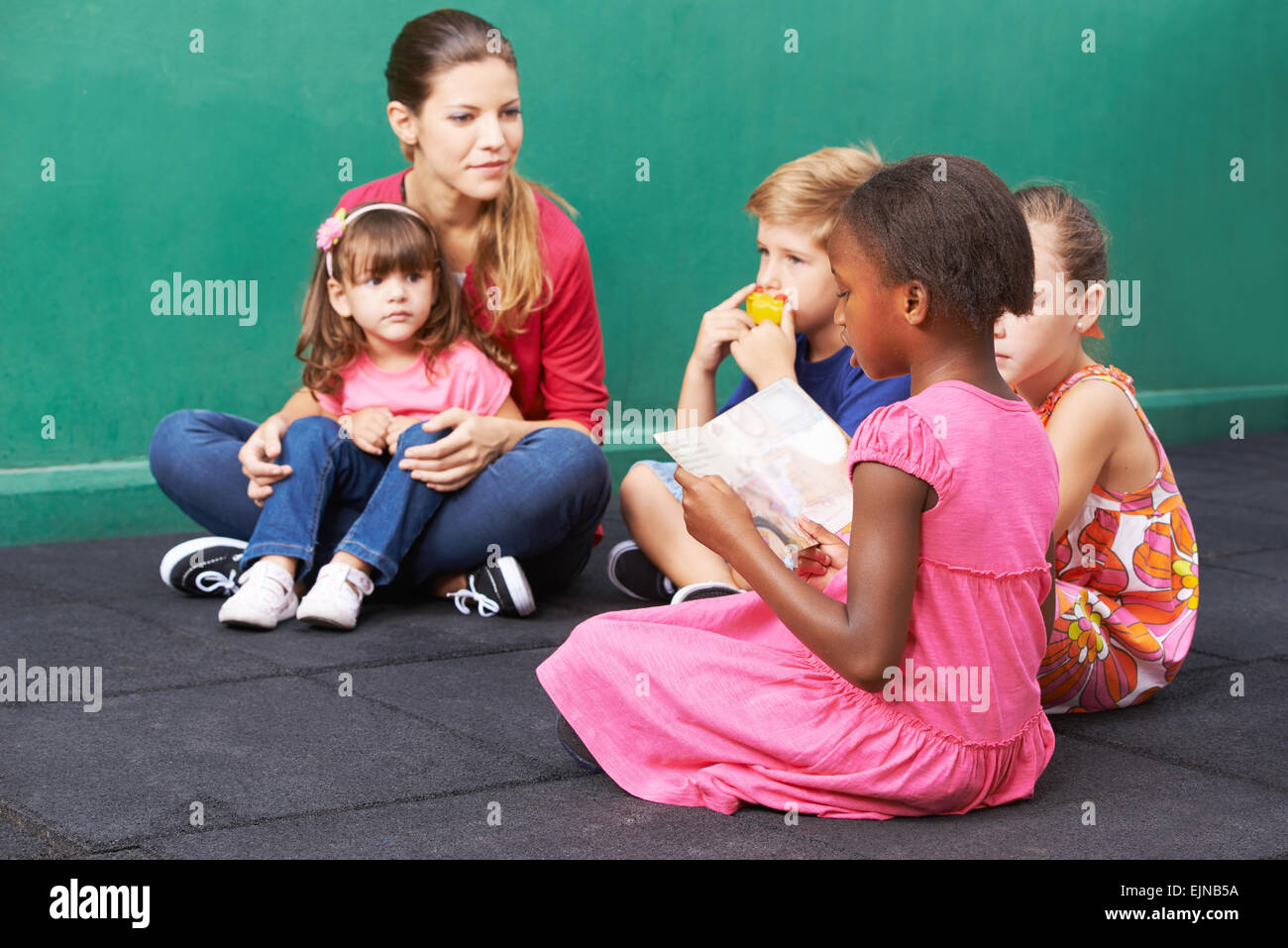 African girl reading aloud for group of children in a kindergarten