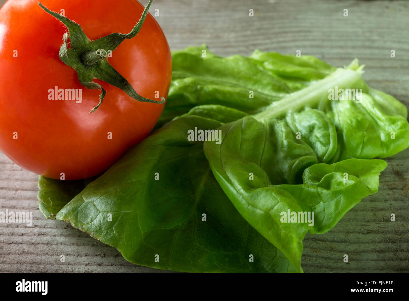 Close up shot of green salad and tomato over wooden background Stock Photo