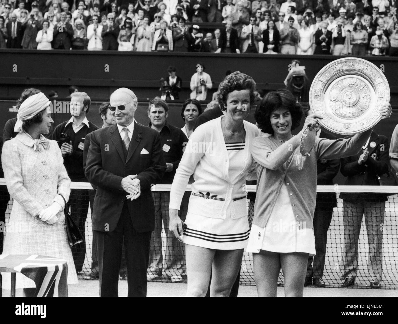 14,000 stamping fans cheered Virginia Wade to victory in her fight against Holland's Betty Stove. Ginny, convinced that she would win received a standing ovation. 'It was like a fairytale,' she said. There was so much noise I couldn't her wat the Queen said'. Our Picture Shows; Virginia Wade with the trophy posing with Betty Stove whilst the Queen chats with a Wimbledon official in the background. 4th July 1977 Stock Photo