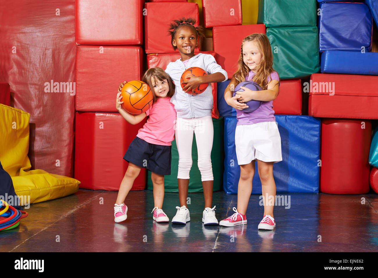 Three happy girls standing with balls in a gym of a preschool Stock ...