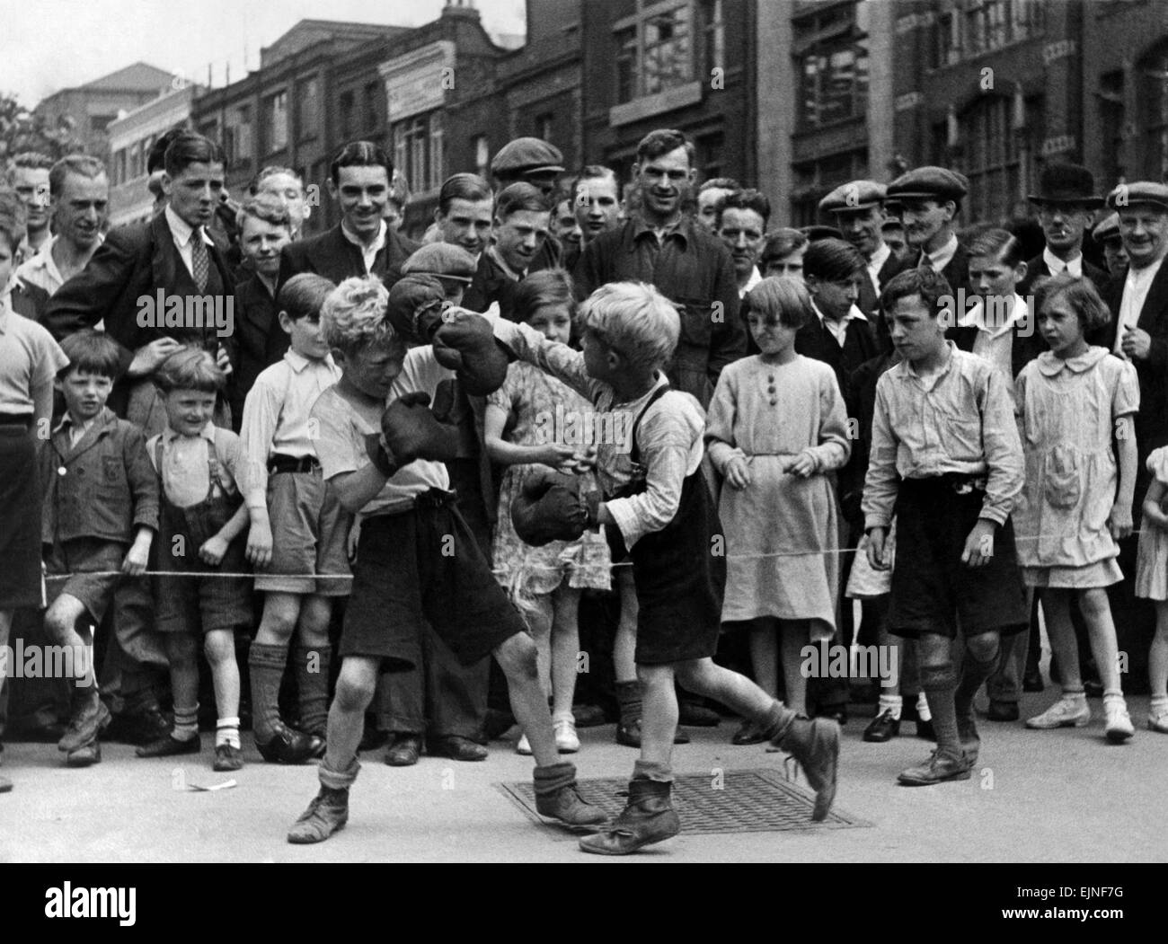 Boxing match in the street at Clerkenwell Green, a company of little boys arranged a boxing match. They set up a ring with a cord. After the performance they collected money (pennies) from the large crowd which was attracted. The boys have performances of several fights. July 1936 Stock Photo