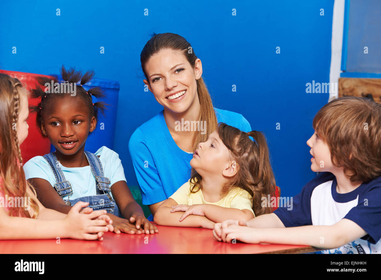 Happy nursery teacher with group of children at a table in kindergarten
