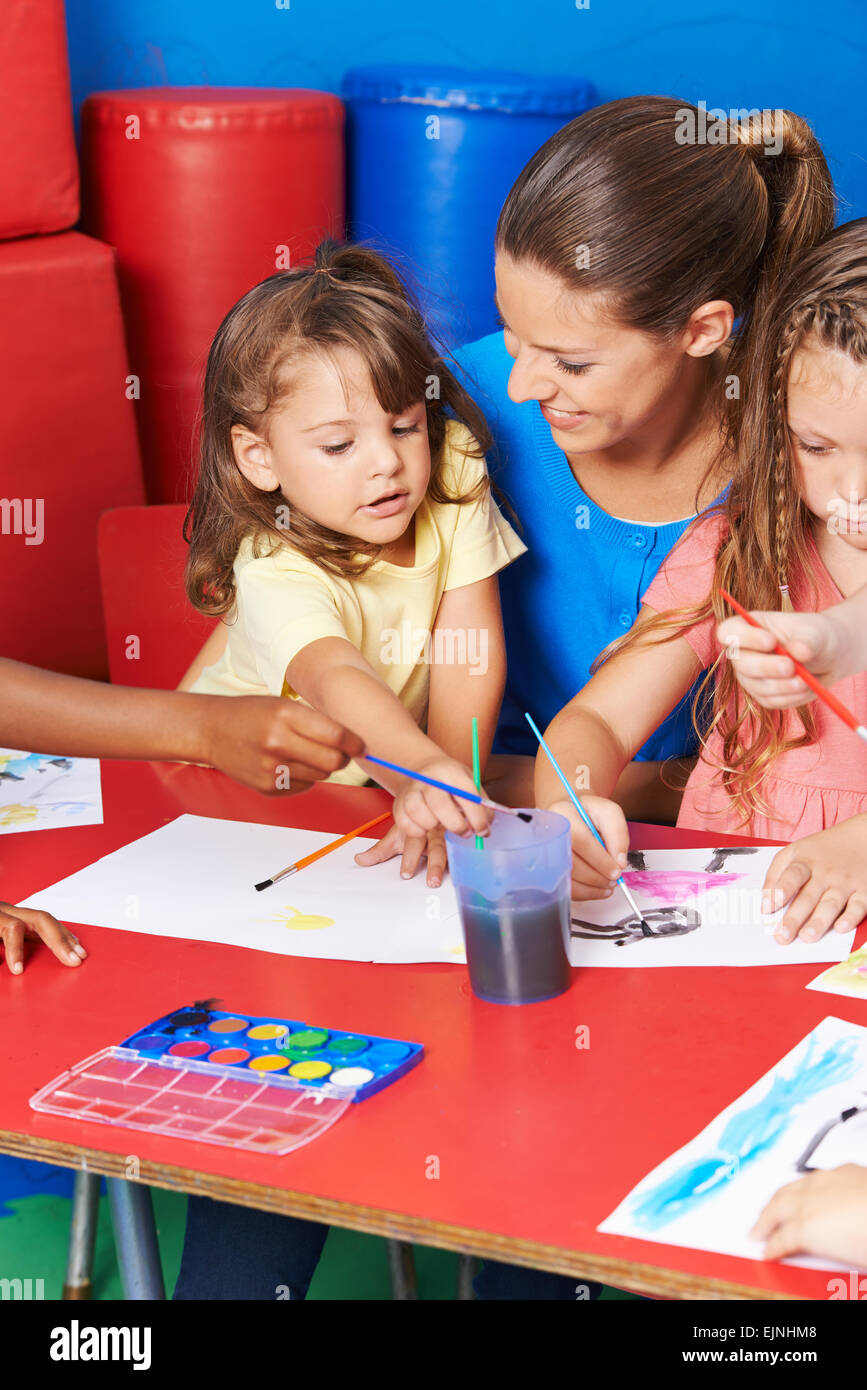 Children painting images in child care after elementary school with teacher Stock Photo