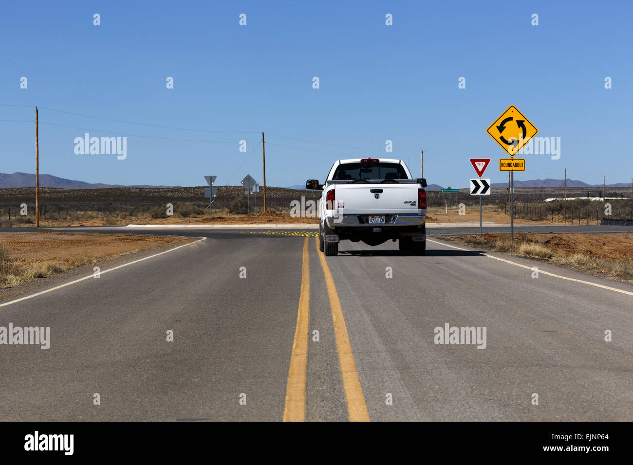 Rear view of a large white Dodge Ram Truck approaching a roundabout located in the middle of a deserted section of road in New Mexico USA Stock Photo