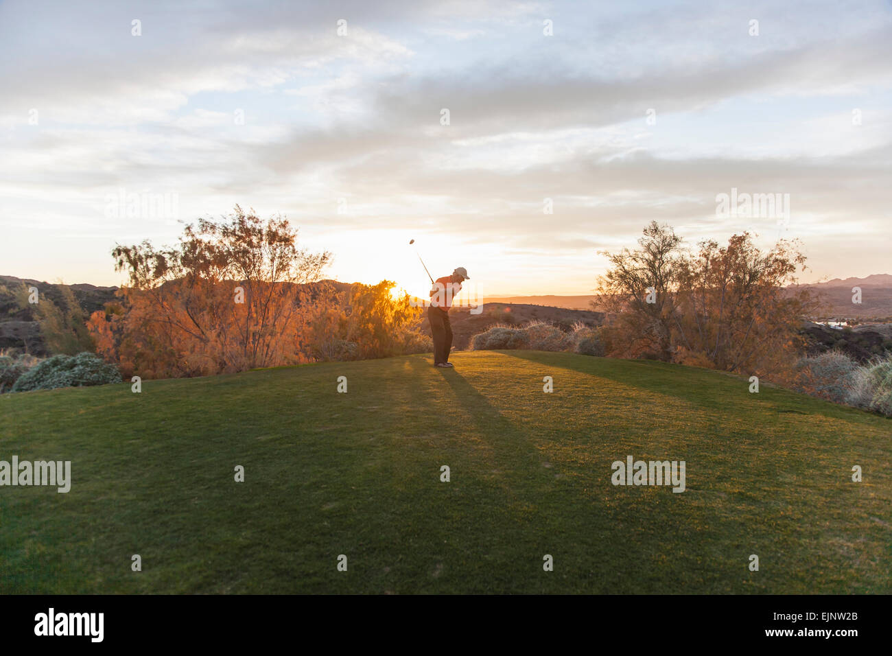 A man taking a shot off a golf tee on a golf course into the sunset. Stock Photo