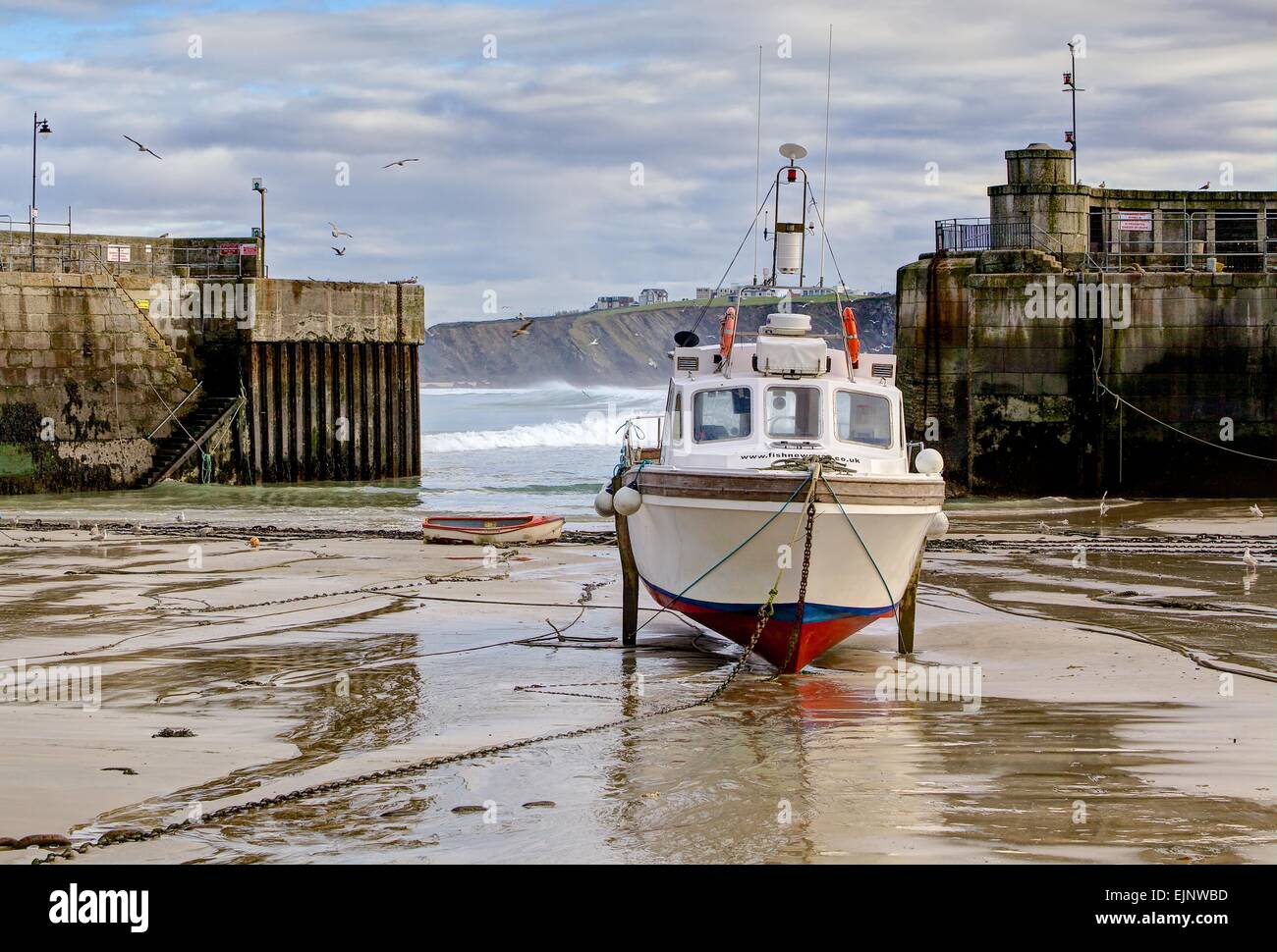 Single boat moored by chain in the safety of a fishing harbour, tides out,  and with views of the coast Stock Photo - Alamy