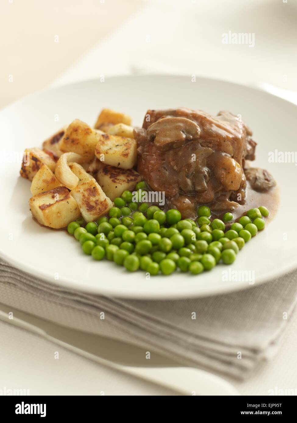 meal of Chicken in red wine and mushroom sauce with peas and fried new potatoes Stock Photo