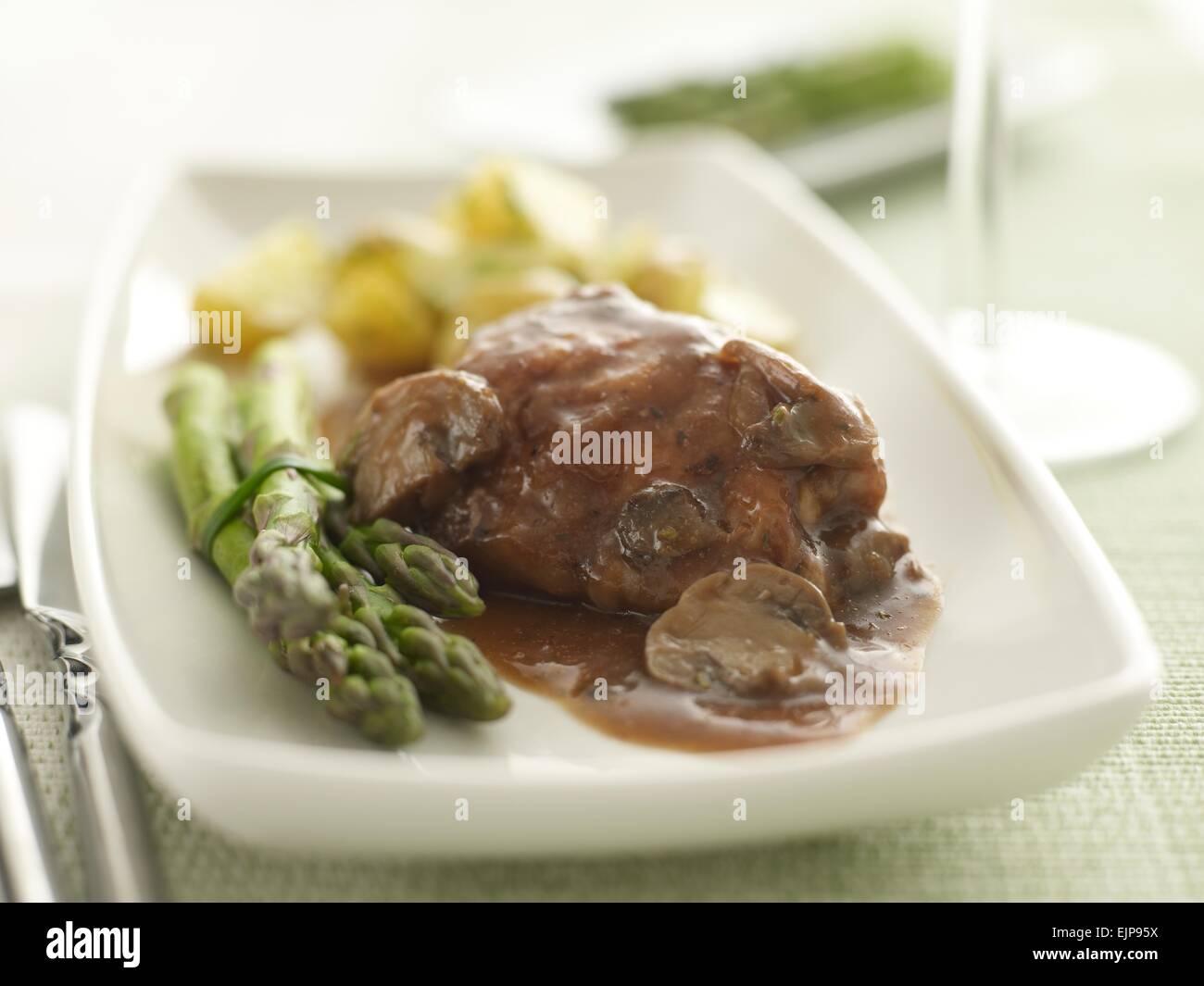 meal of Chicken in red wine and mushroom sauce with asparagus tips and new potatoes Stock Photo