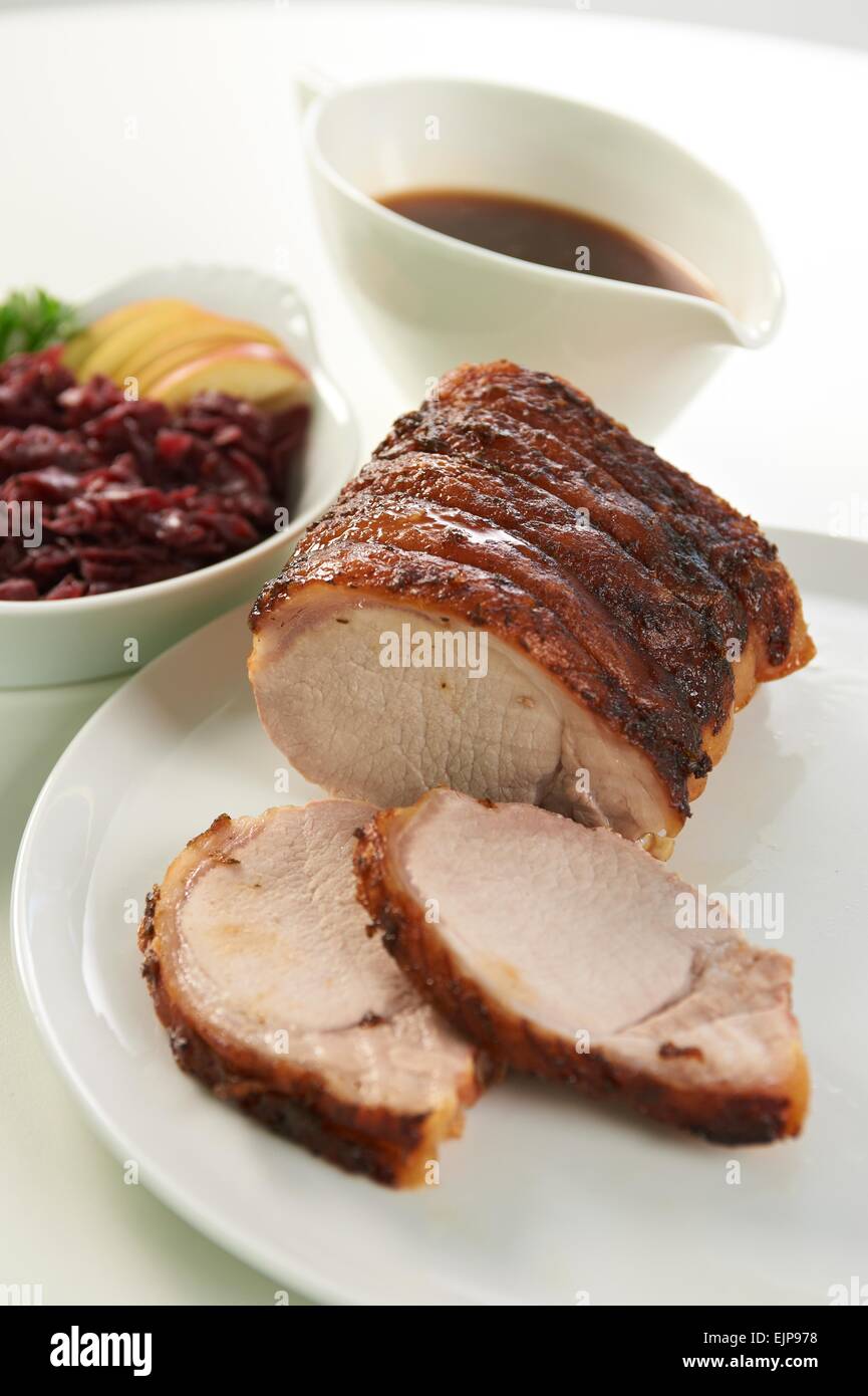 Sunday roast pork lunch gravy boat red cabbage apple slices crackling round white plate Stock Photo