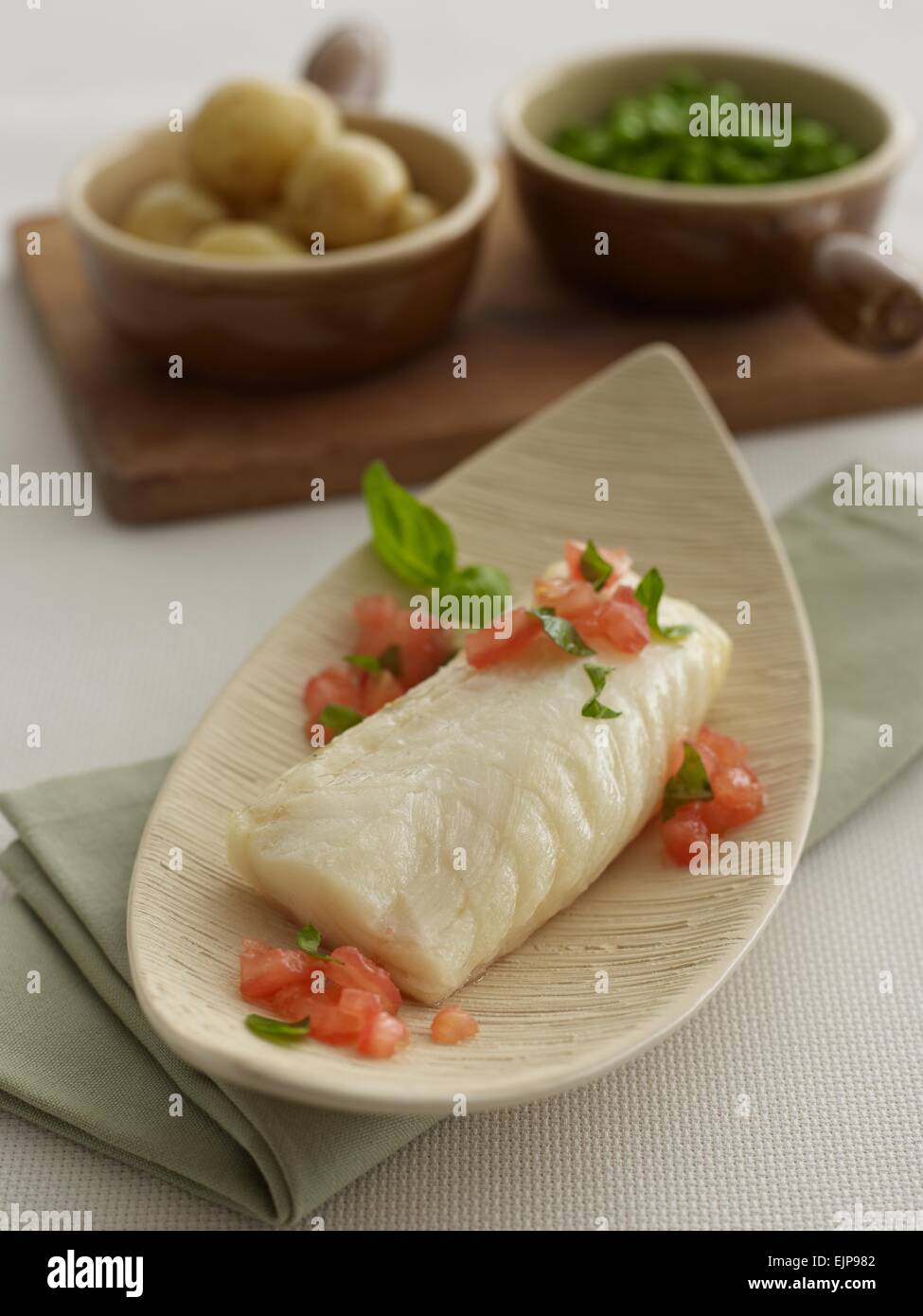 Simple plated meal of pan fried plain fillet of haddock or cod fish with chopped tomato and basil boiled new potatoes Stock Photo
