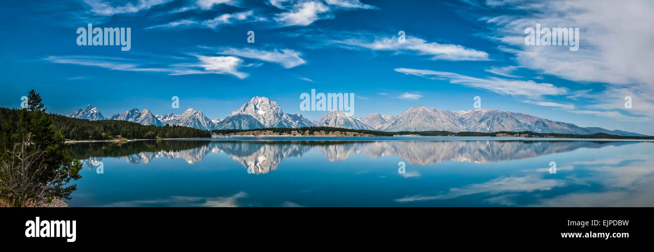 Panoramic image of stunning mirror-like reflections of the Grand Tetons in Jackson Lake, Wyoming, USA with azure blue skies and water Stock Photo