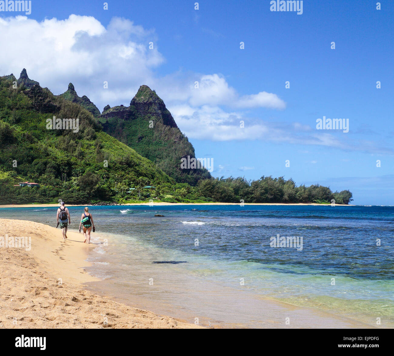 Couple carrying snorkel gear walk along shoreline in Haena, Kauai, after snorkeling at Tunnels Beach Stock Photo