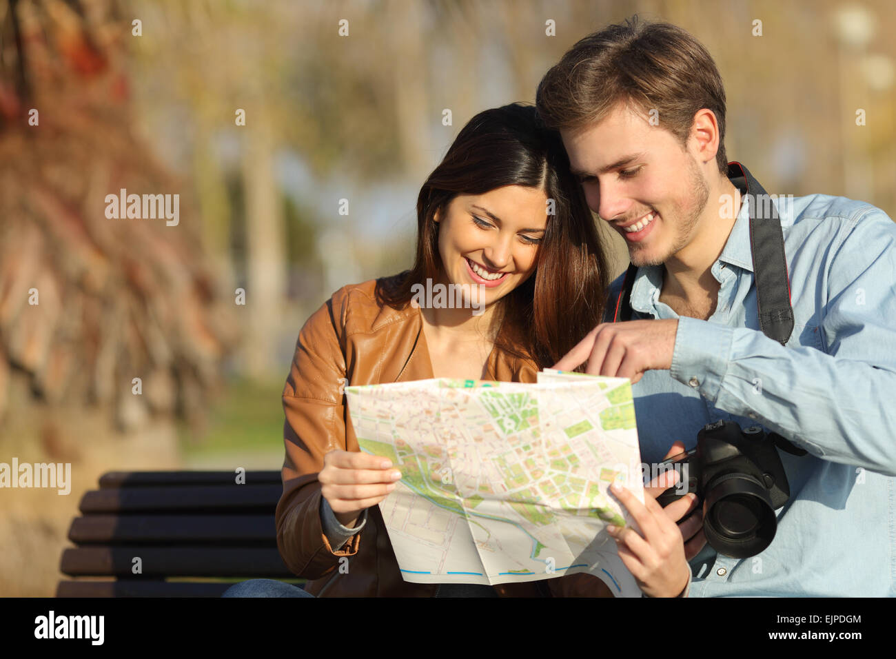 Happy tourists searching landmarks in a map sitting on a bench outdoors Stock Photo