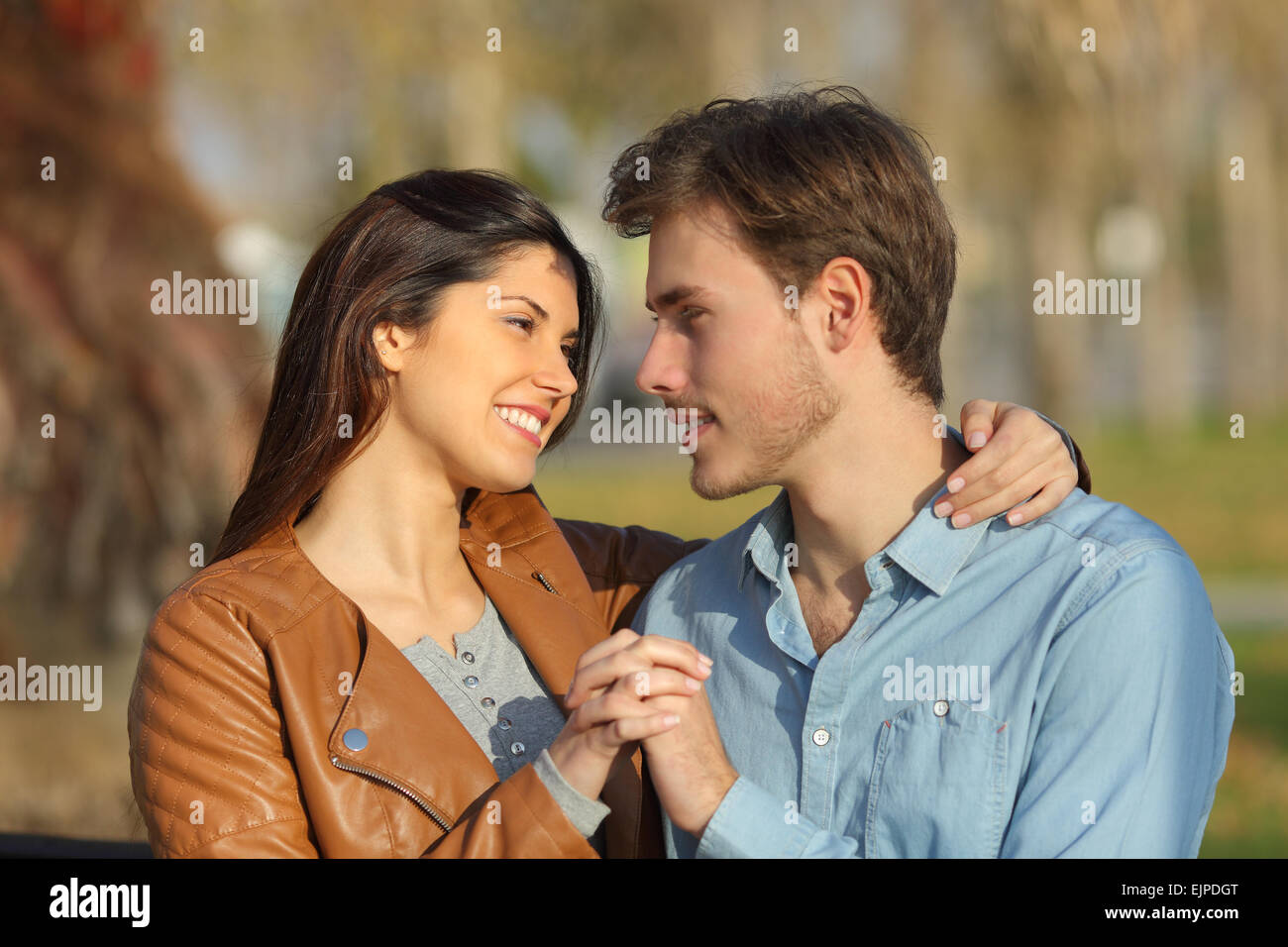 Couple in love hugging and dating sitting on a bench in a park looking ...