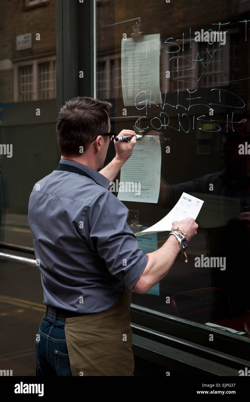 Waiter writing menu on restaurant window Stock Photo