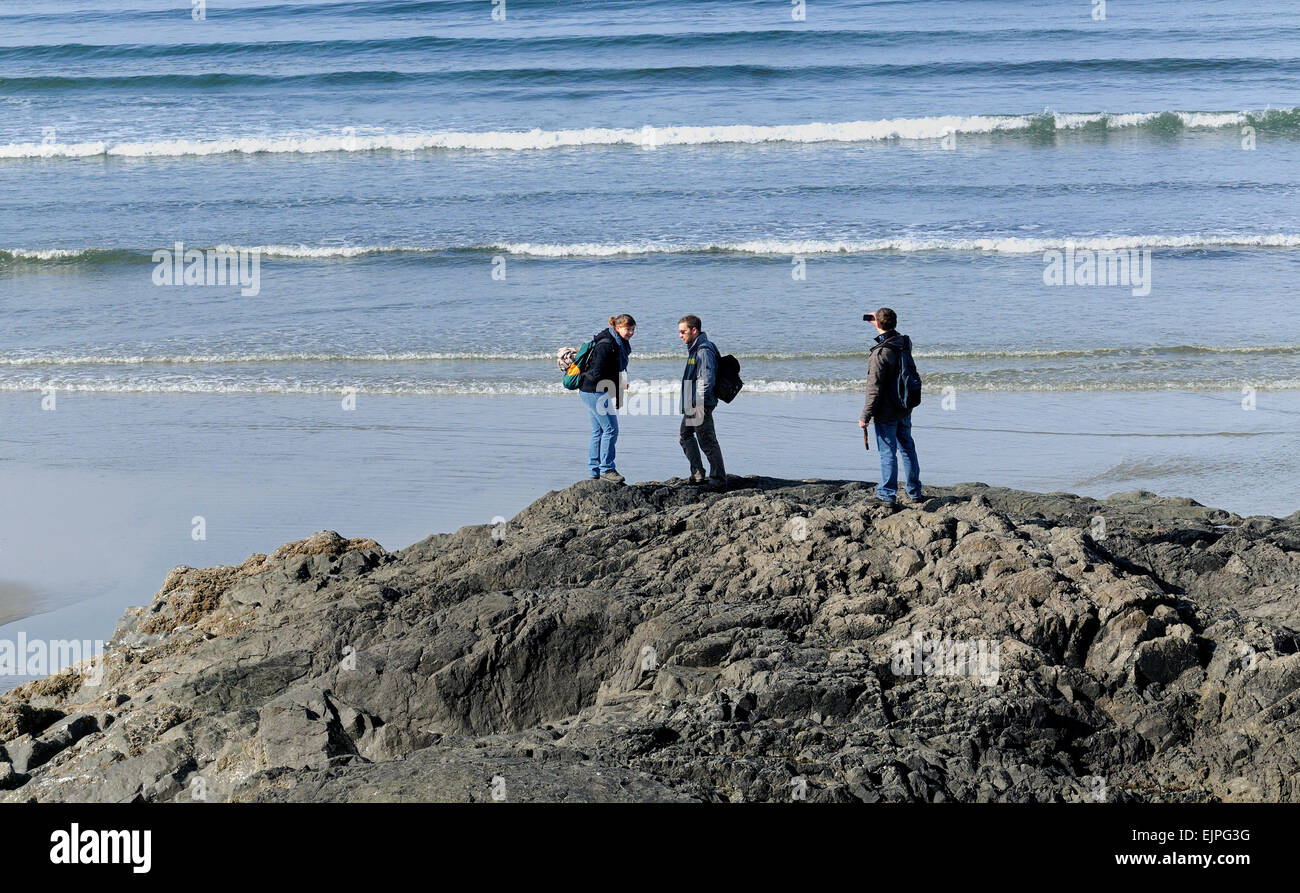 Three people on a rock on Wickaninnish Beach, Pacific Rim National Park. Stock Photo