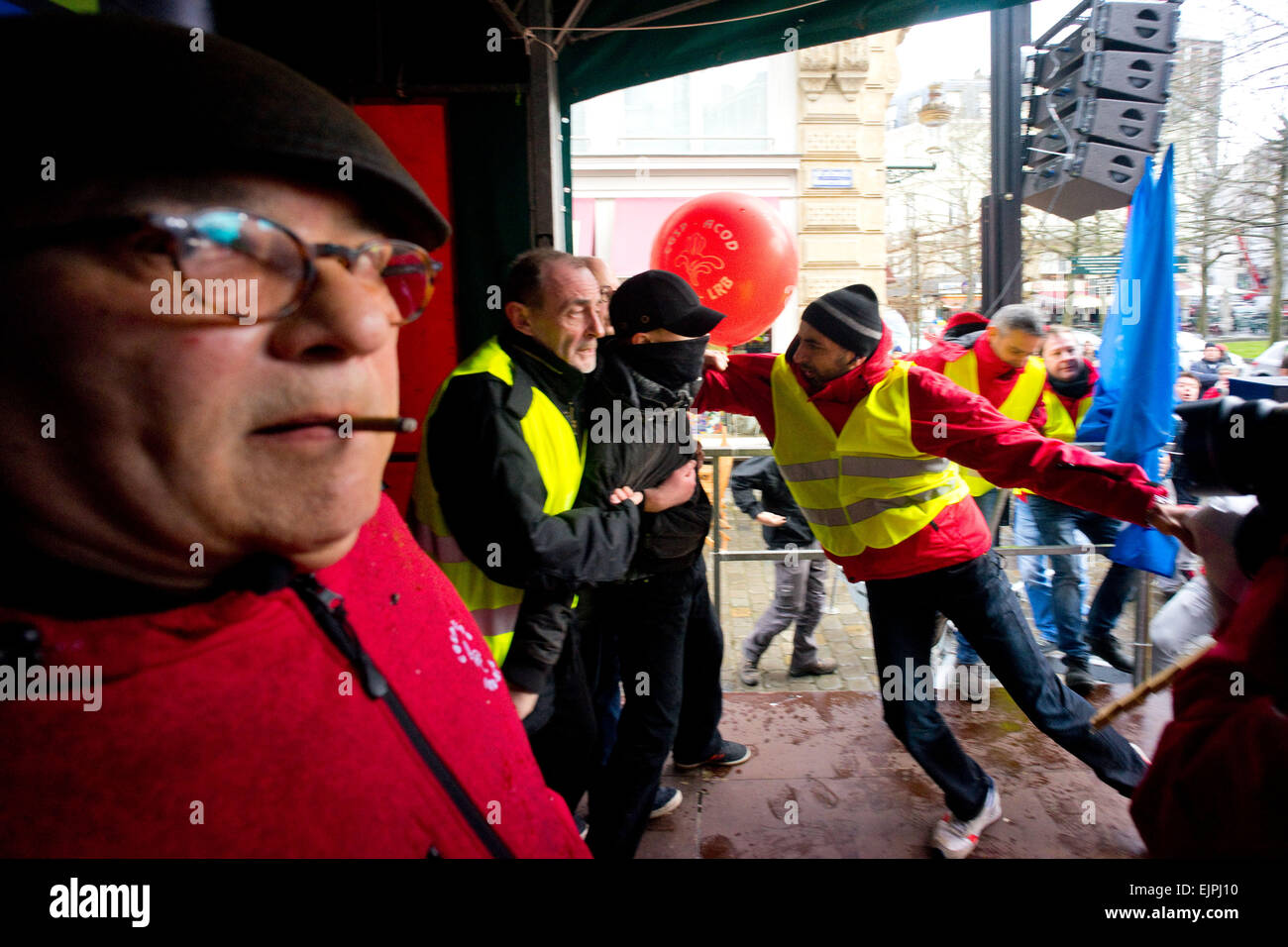Brussels, Belgium. 30th Mar, 2015. A masked man tries to disrupt an union union leader's speech by storming the stage, he was being taken away by the security team. - Thousands took part in an anti austerity demonstration organized by multiple workers' unions and political parties. Clash broke out as members of 'LCR' (Revolutionary Communist League of Belgium) tries to take over the stage. Credit:  Geovien So/Pacific Press/Alamy Live News Stock Photo