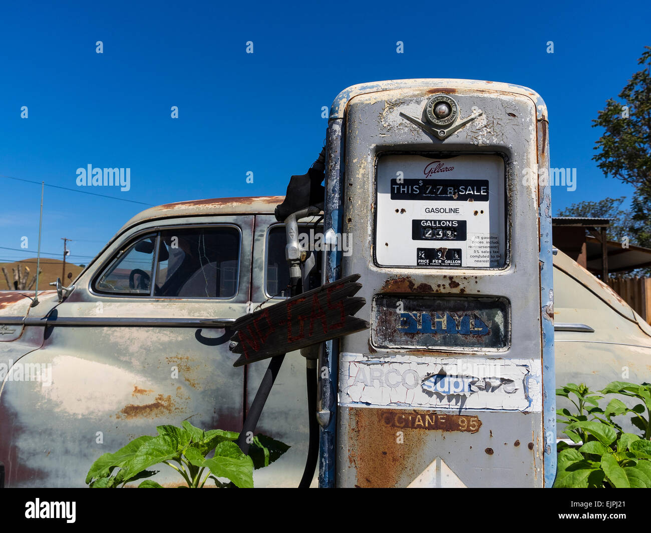 A 1947 Chrysler 4-door sedan rusting with faded paint sits parked in front of two old style gas pumps at a filling station. Stock Photo