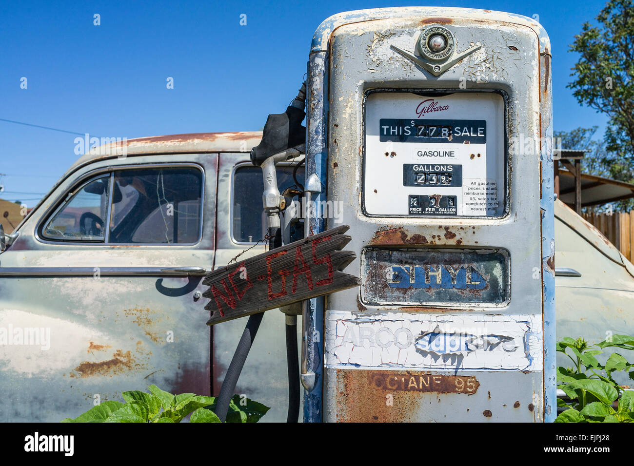 A 1947 Chrysler 4-door sedan rusting with faded paint sits parked in front of two old style gas pumps at a filling station. Stock Photo