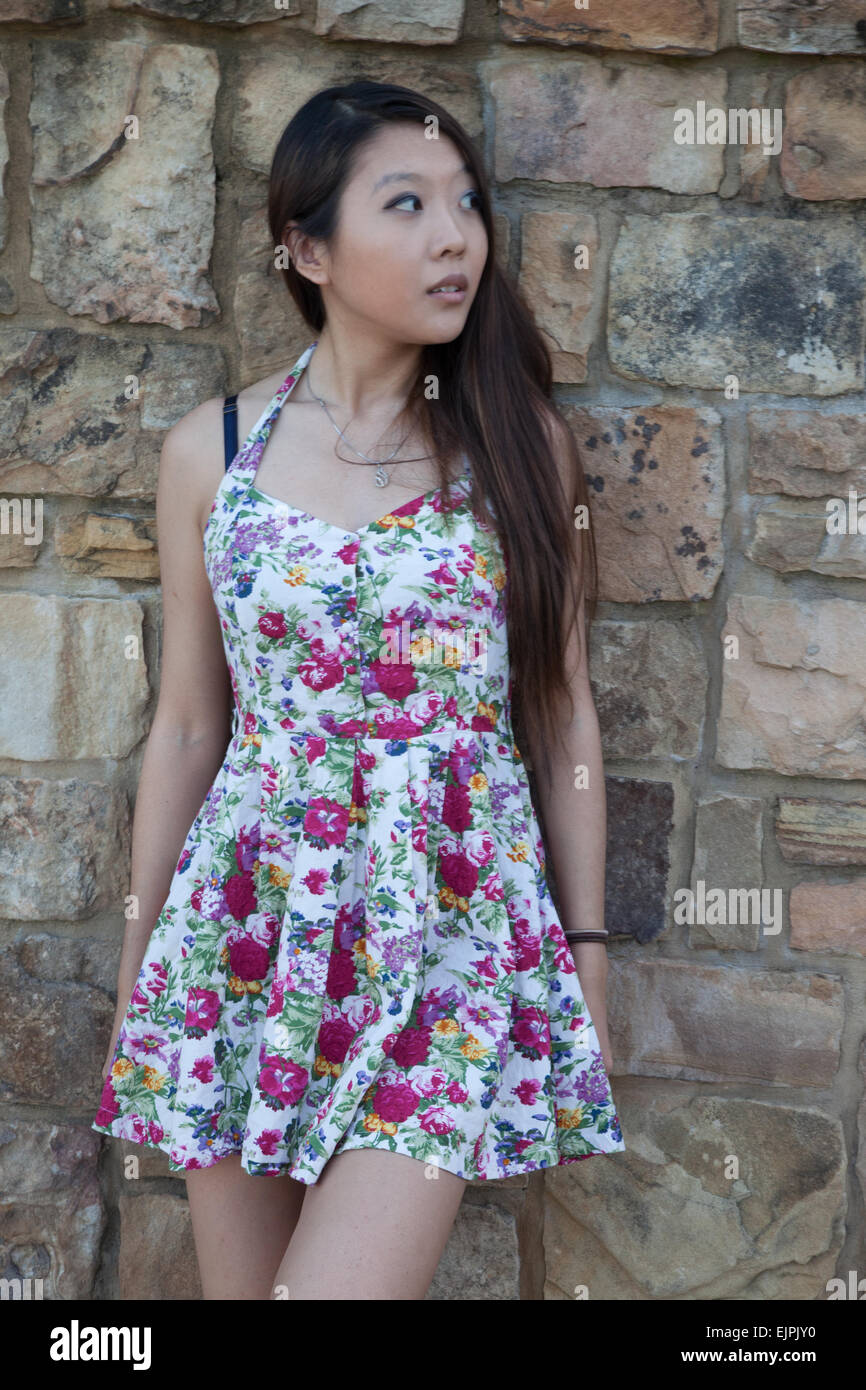 Pretty Asian woman outdoors in a flowered dress, looking thoughtful Stock Photo