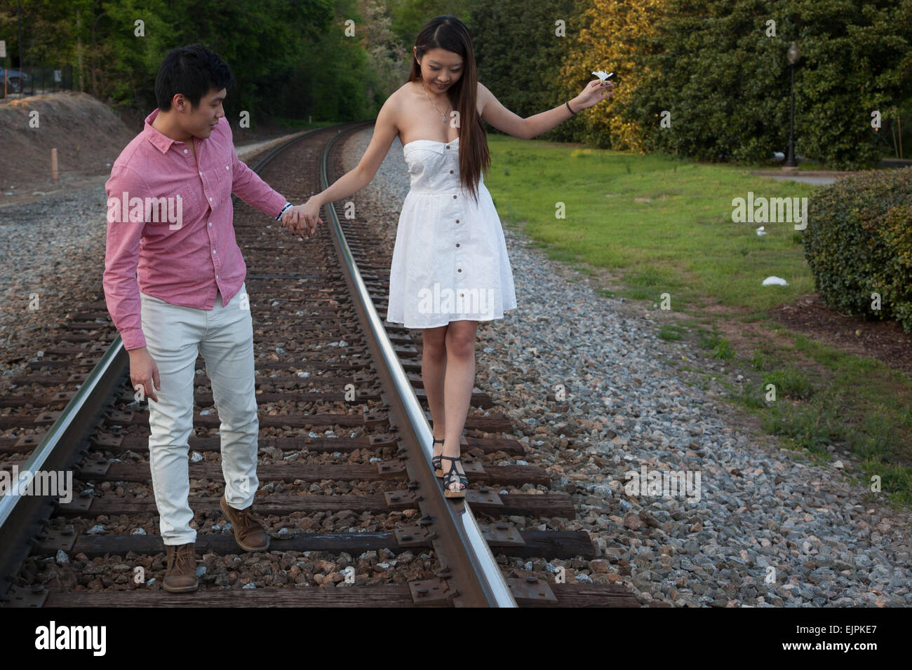 Romantic Asian couple playing outside on railroad tracks, being affectionate and smiling Stock Photo