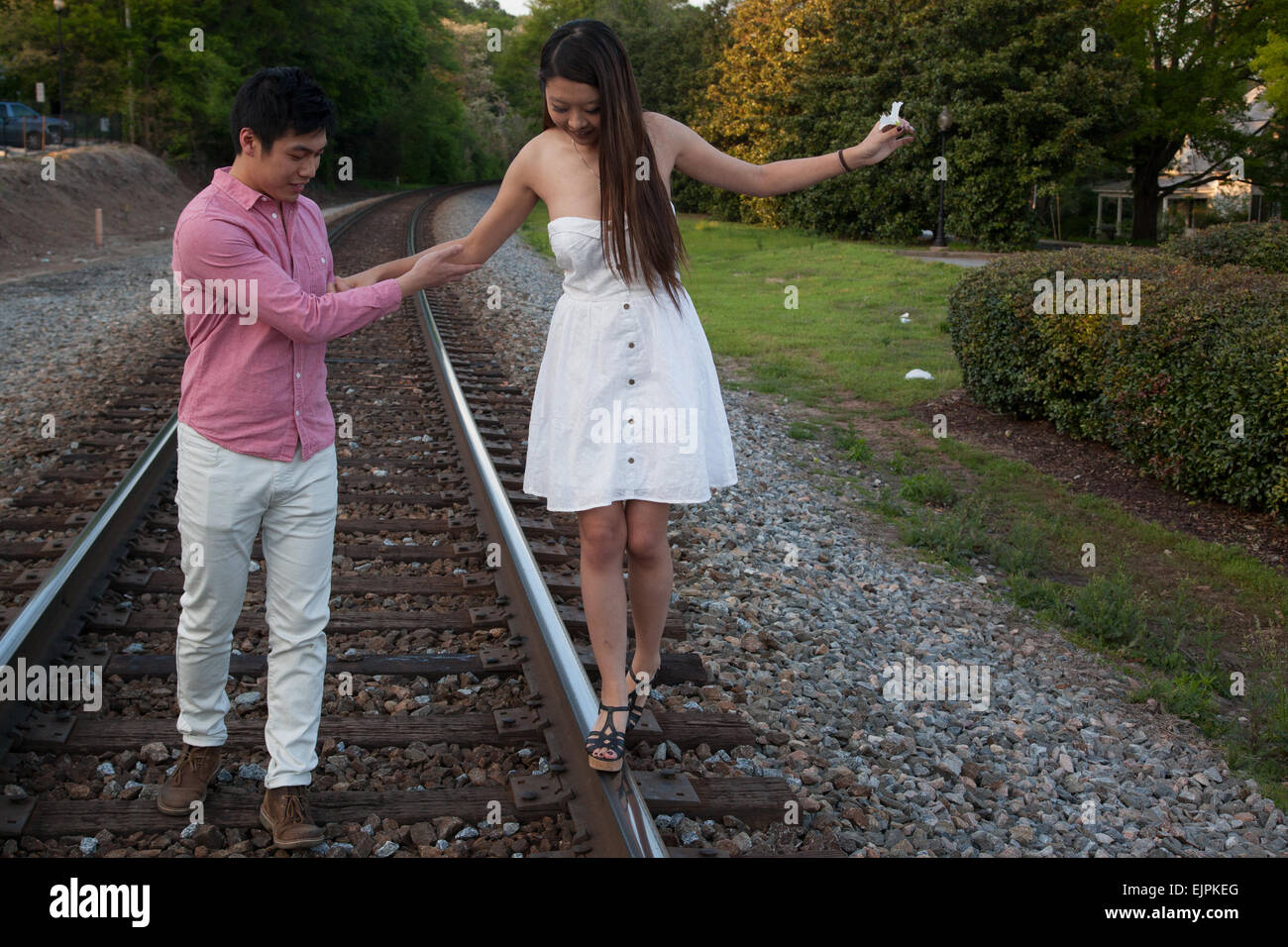 Romantic Asian couple playing outside on railroad tracks, being affectionate and smiling Stock Photo