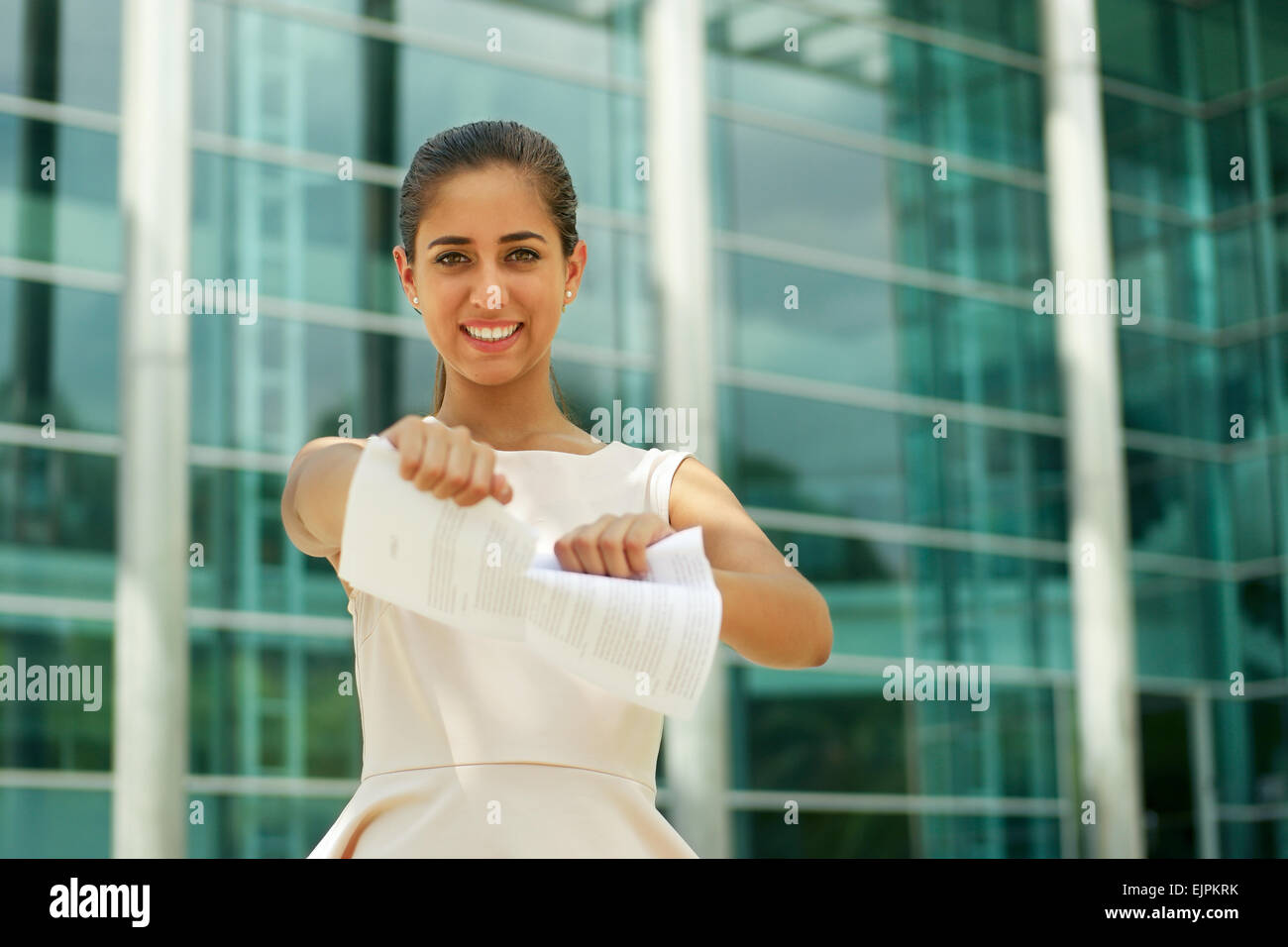 Portrait of beautiful latina businesswoman resigns from job, tearing a employment contract and looking happy at camera, smiling Stock Photo