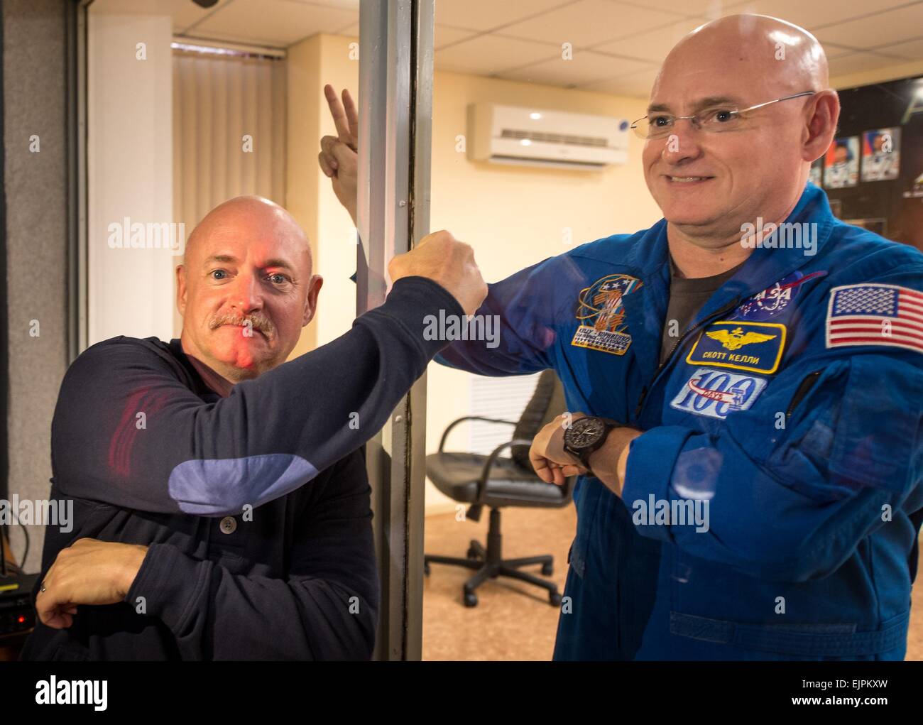 International Space Station Expedition 43 Commander NASA Astronaut Scott Kelly waves to his identical twin brother former NASA astronaut Mark Kelly behind glass during the crew press conference at the Cosmonaut Hotel March 26, 2015 in Baikonur, Kazakhstan. Kelly and cosmonauts Mikhail Kornienko and Gennady Padalka launch in their Soyuz TMA-16M spacecraft on March 28 for a year long mission onboard the ISS. Stock Photo