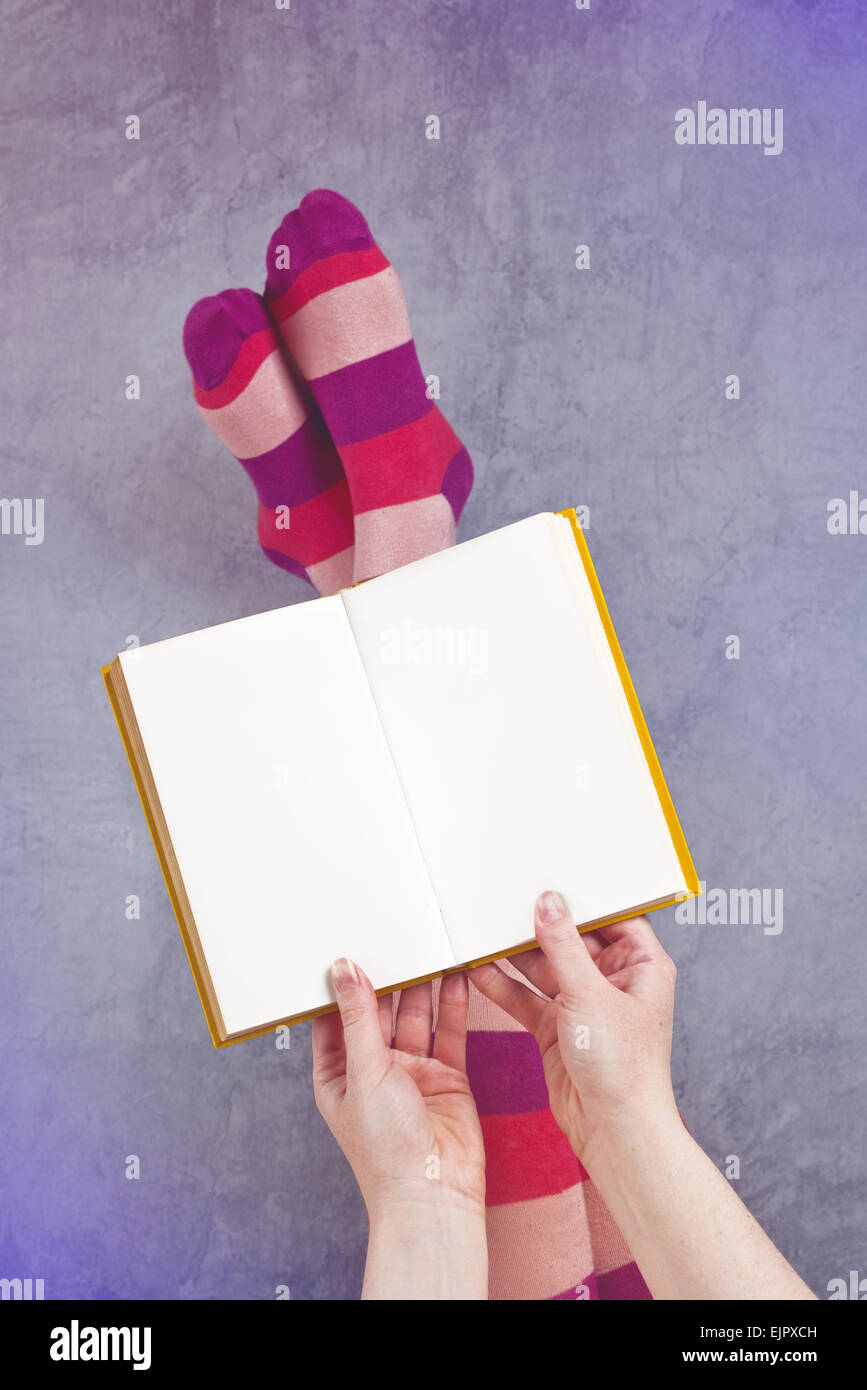 Young Woman Reading Pulp Fiction Book with Her Feet Raised in The Air, Blank Pages as Copy Space. Stock Photo