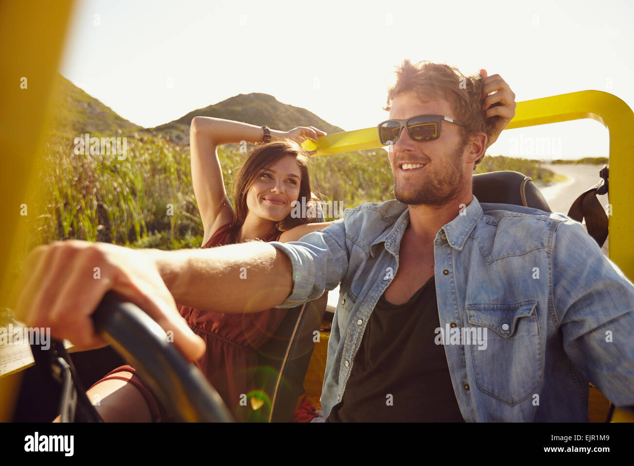 Woman looking at man driving car on a summer day. Loving young couple on road trip. Stock Photo