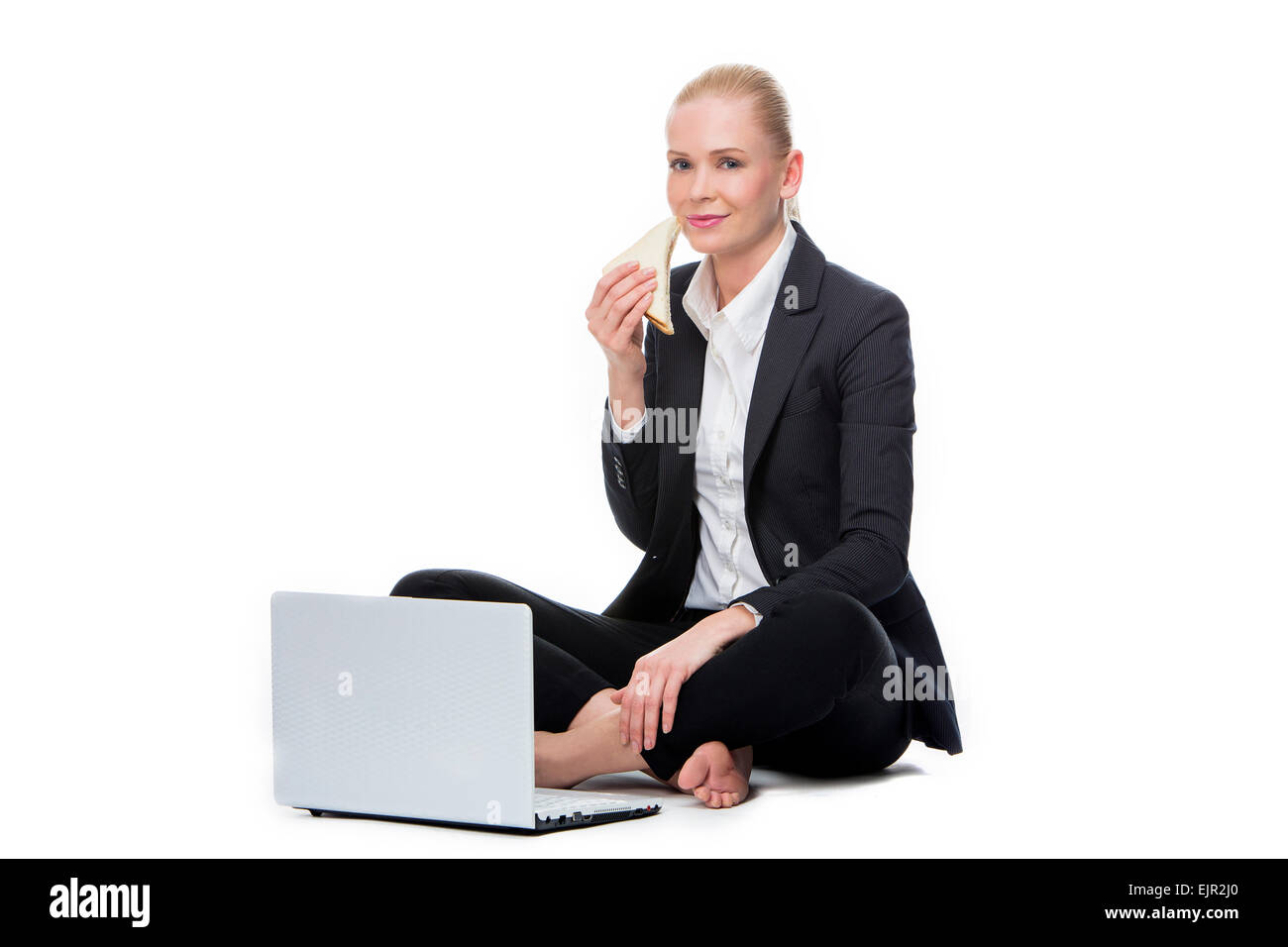 blonde businesswoman seated on the floor with computer and eating a sandwich Stock Photo