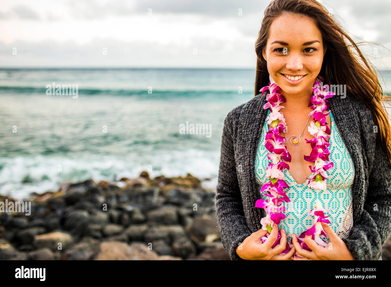 Pacific Islander woman wearing flower lei near rocky beach Stock Photo