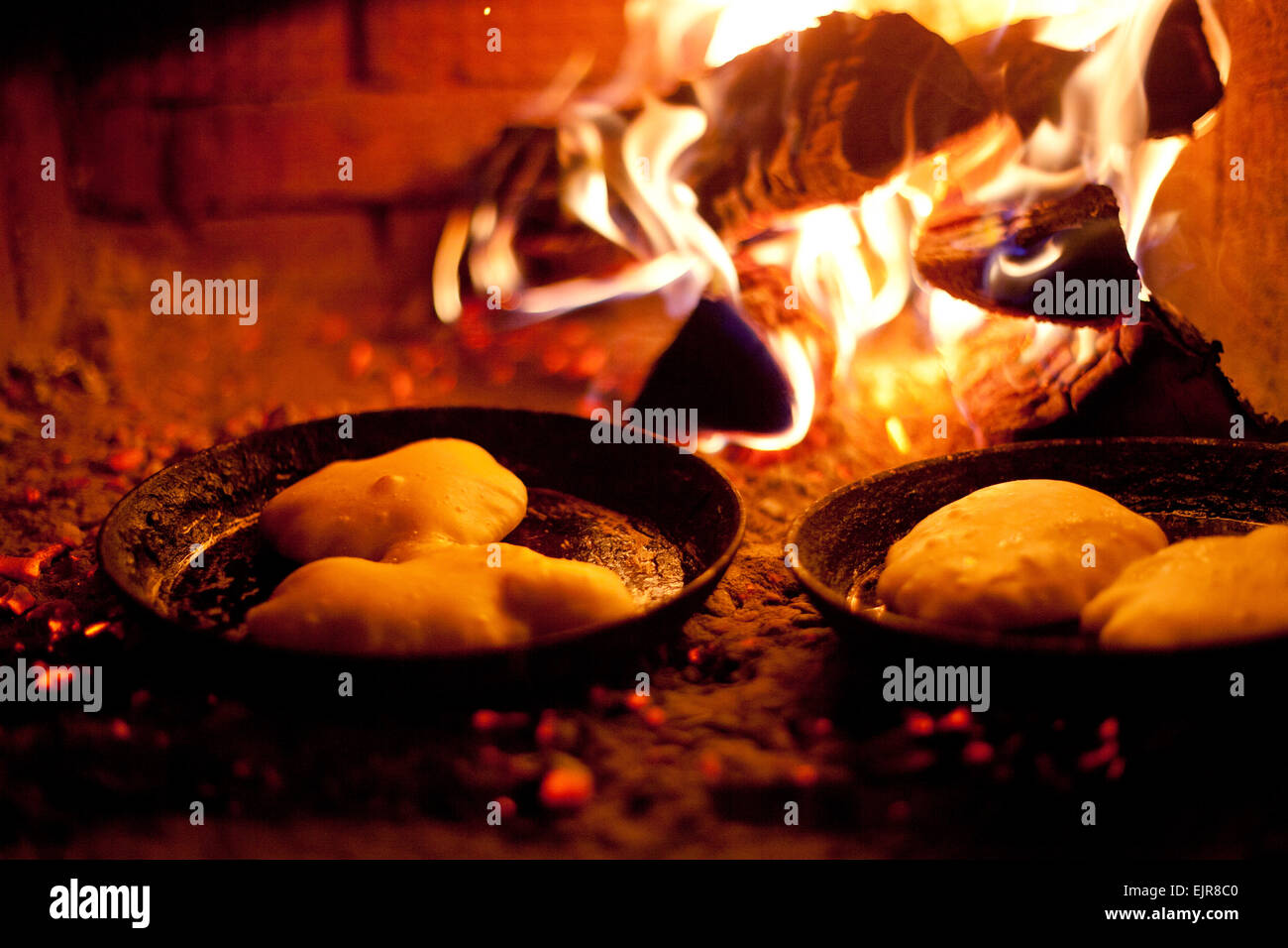 Close up of pastries cooking in skillets near wood fire Stock Photo